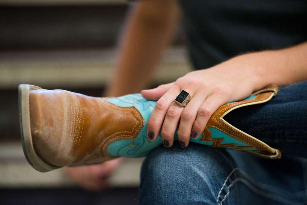 A close-up of an equine student's cowboy boot with her hand and Woods Ring holding onto it.